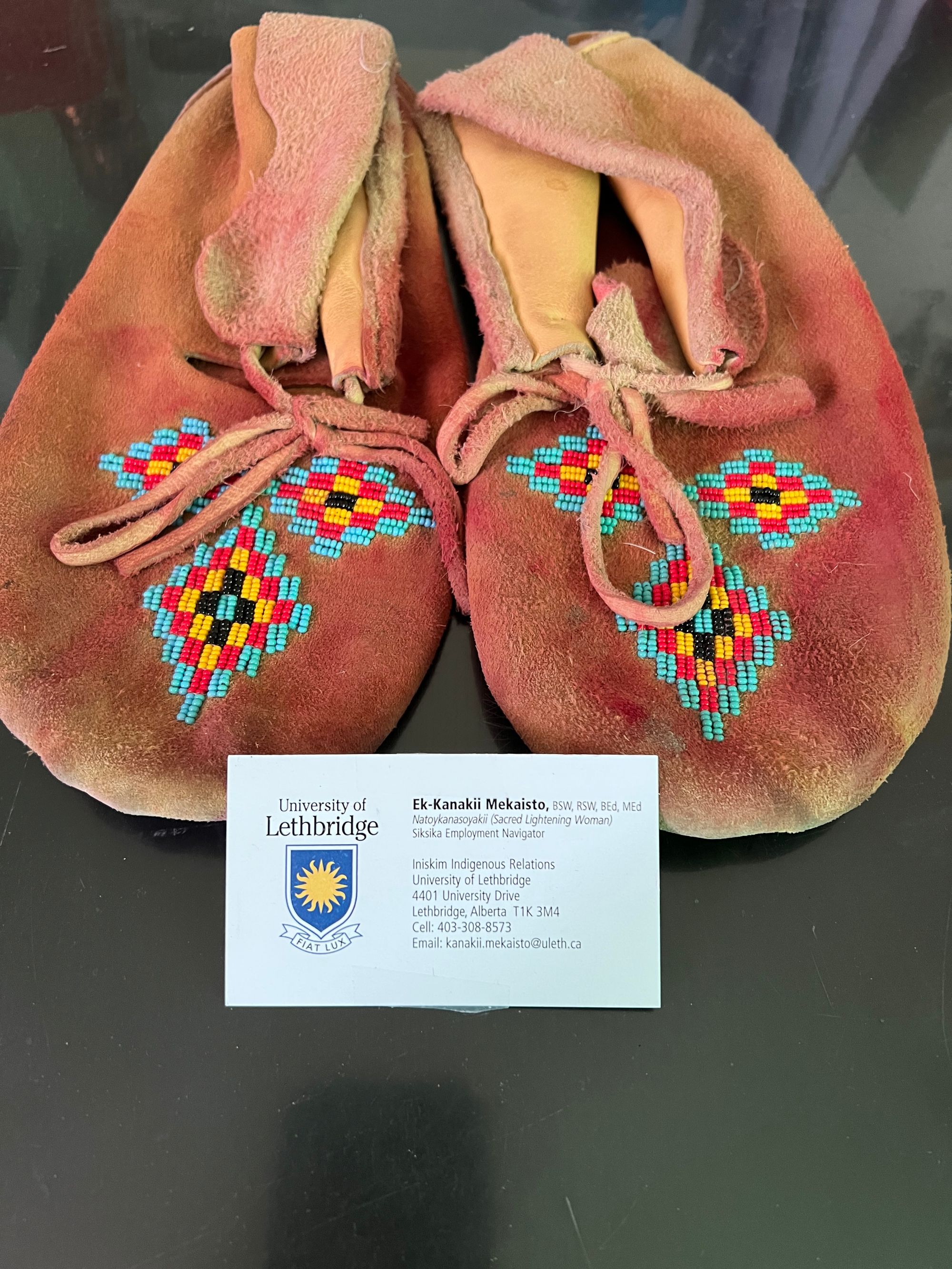 A pair of brown and red moccasins with a business card on top.