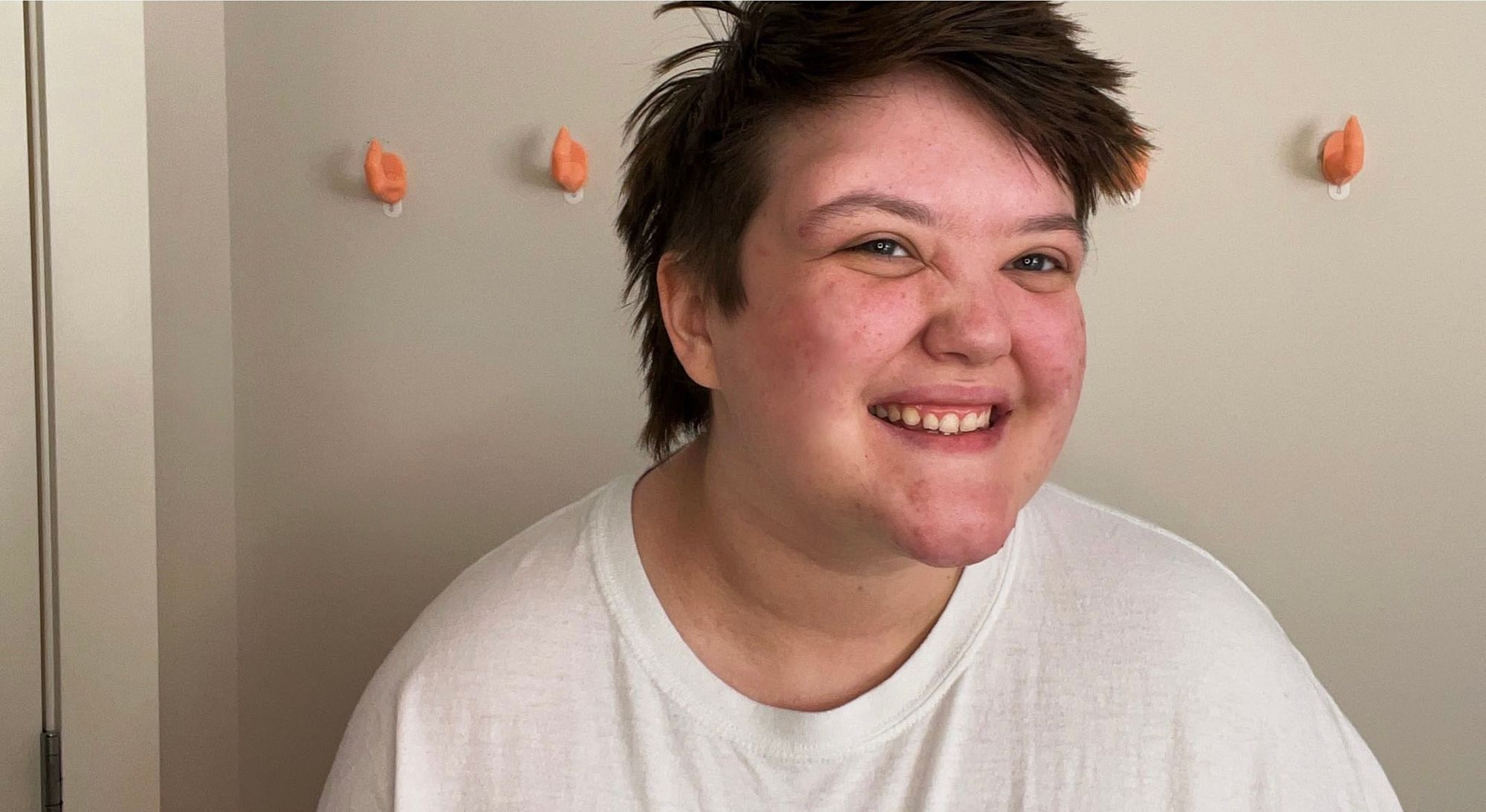 A young person with short hair and wearing a white shirt smiles.