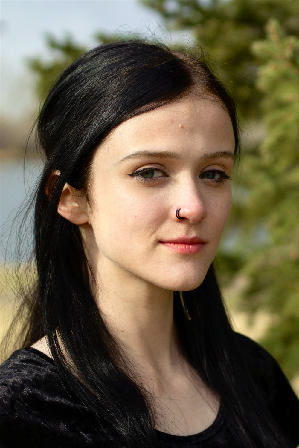 Close-up portrait, young woman with black hair and a black shirt, two black nose rings.