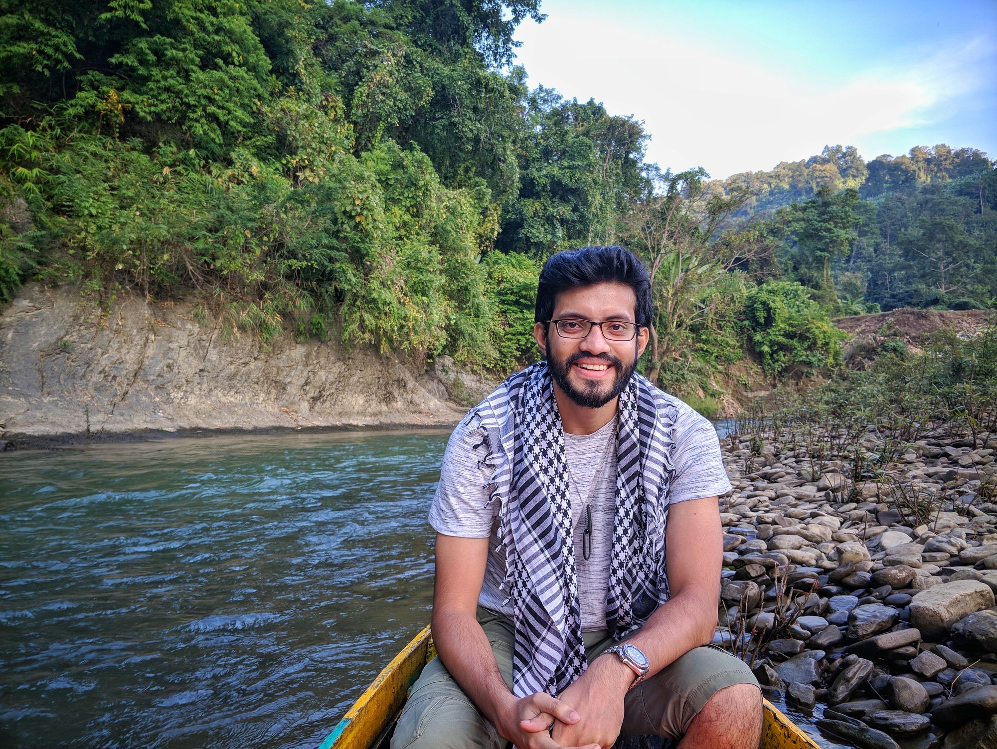 A person on a boat floating down a river with glasses, short hair, and patterned scarf.
