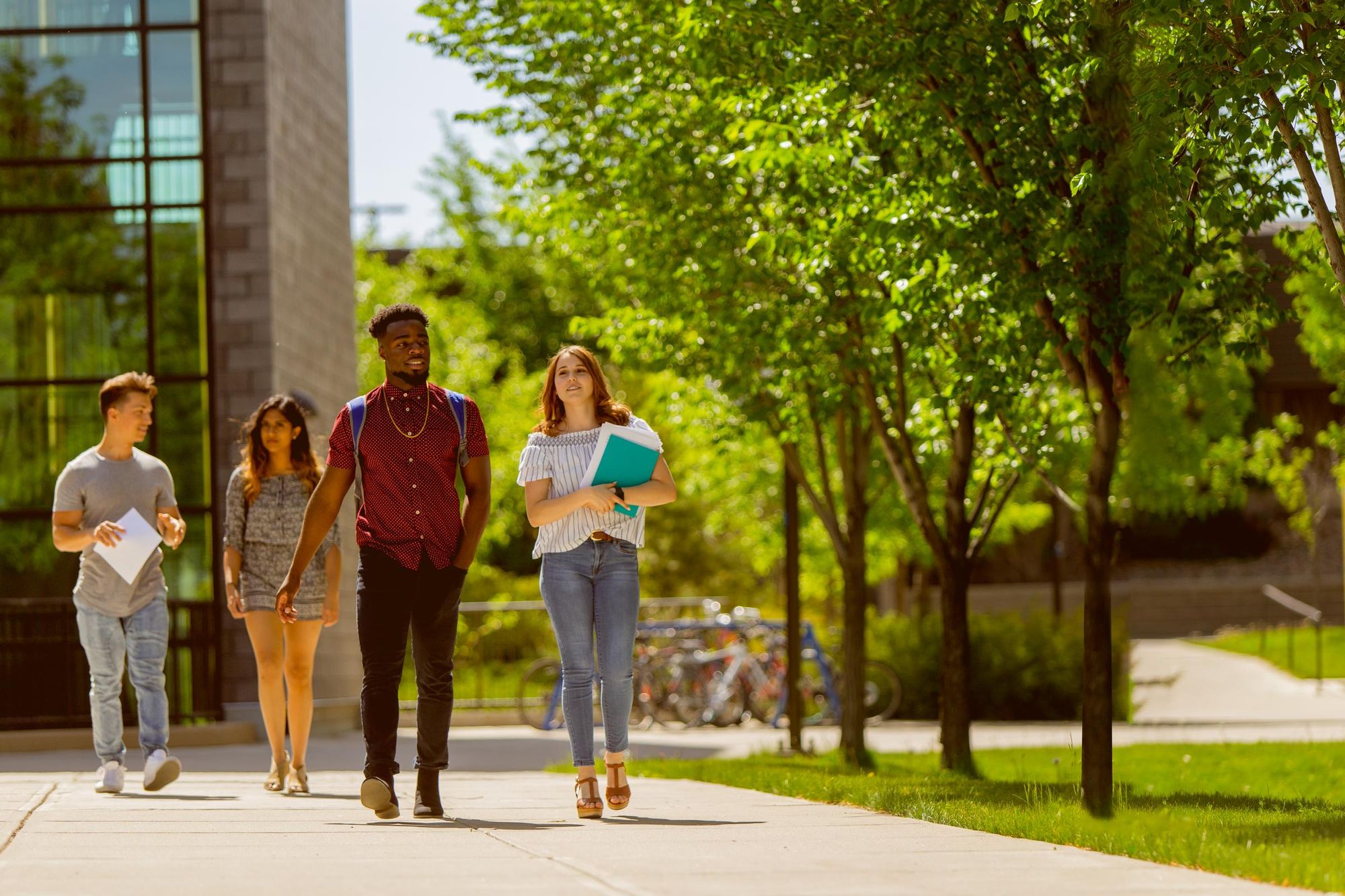 Four students walking alongside green grass and leafy trees on ULethbridge campus