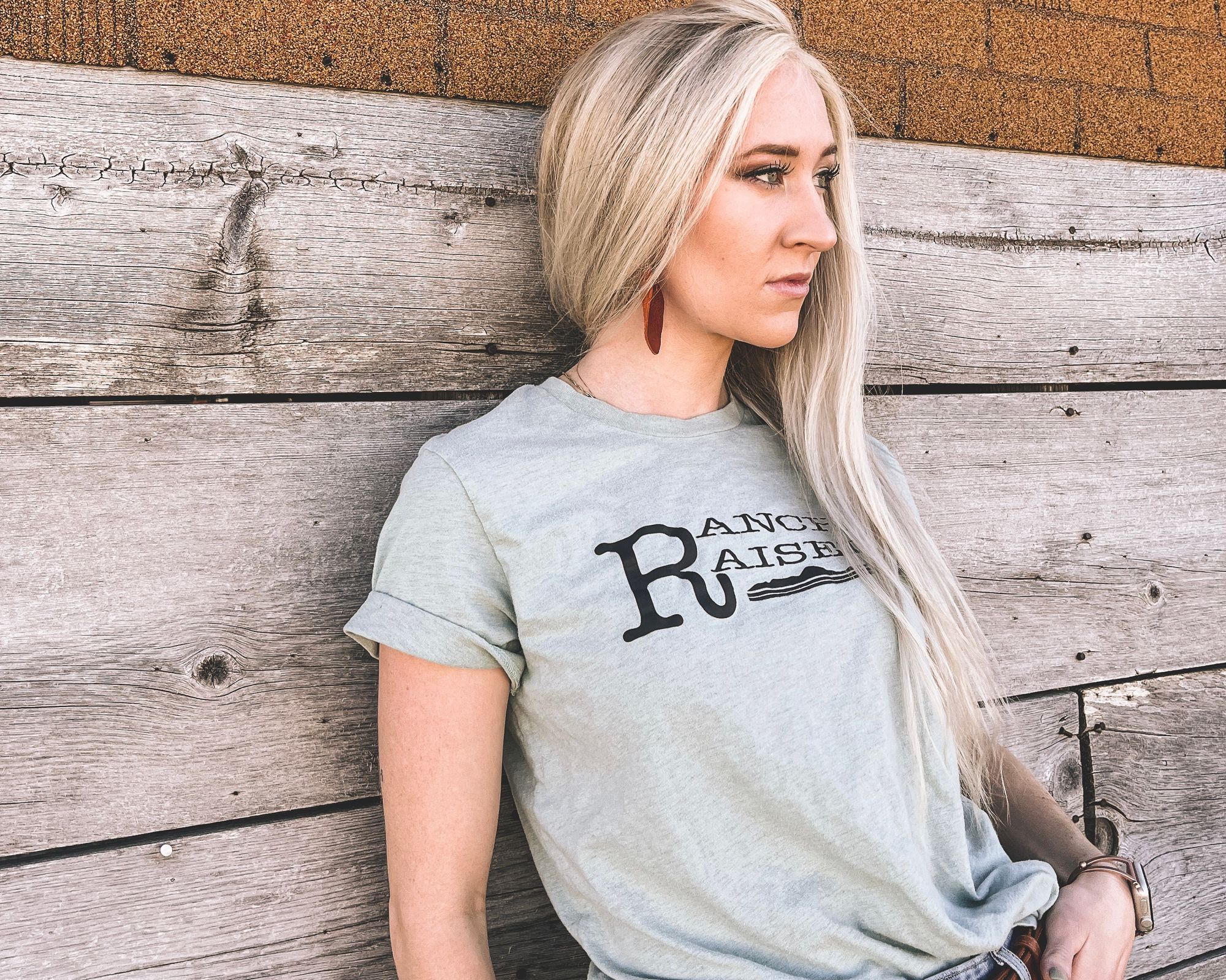 Victoria Steffensen leaning against wood boards, wearing a shirt that reads Ranch Raised.