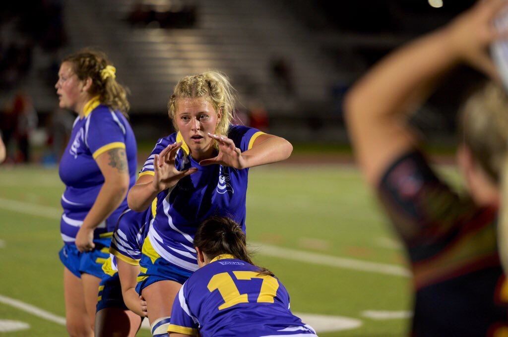 Women in blue and yellow uniforms playing rugby.