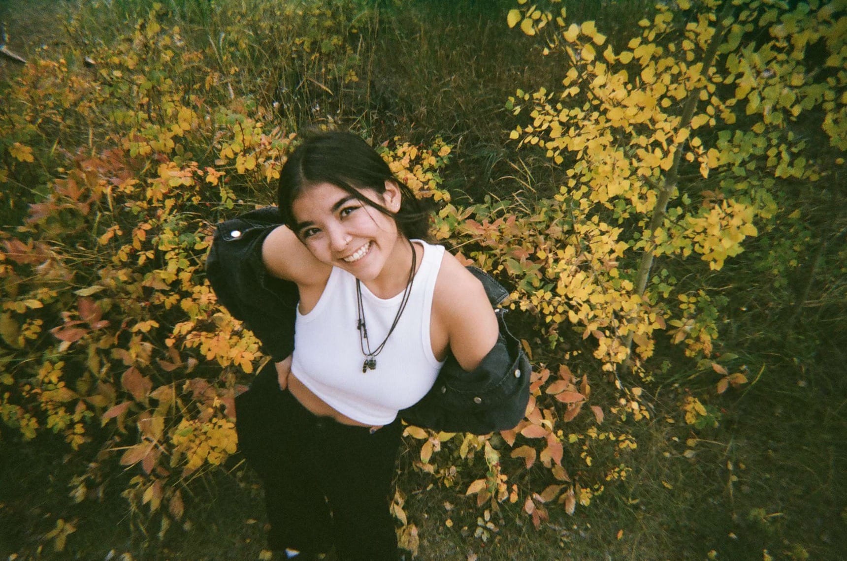 Student smiling and standing in front of shrubs with yellow and orange leaves